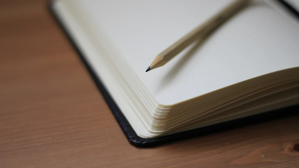Cuaderno abierto por una página en blanco con un lápiz apoyado encima