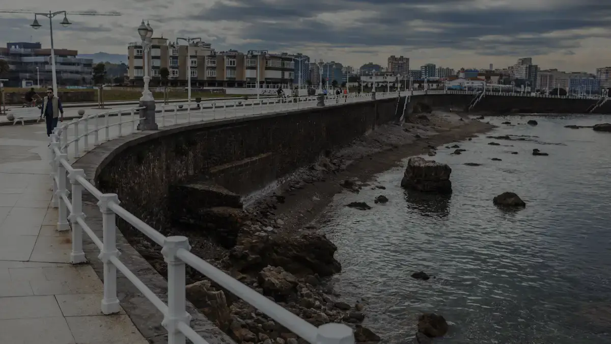Paseo del Muro de San Lorenzo en Gijón, con la barandilla blanca y la ciudad al fondo